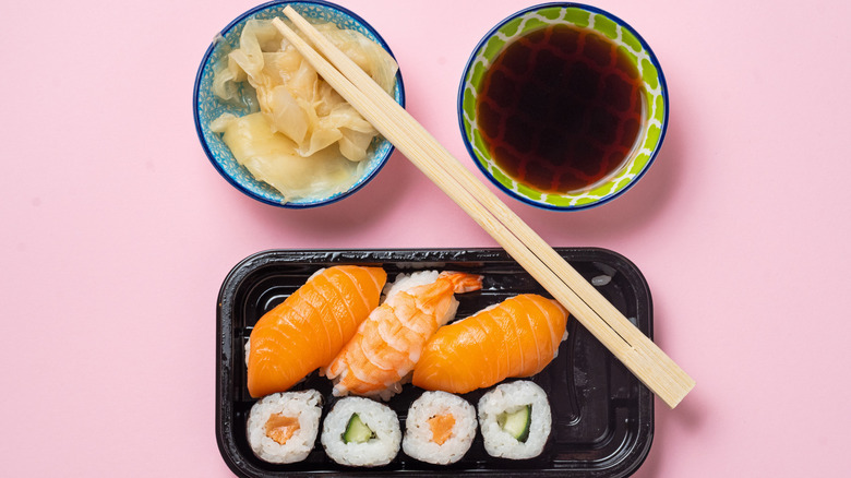 A bowl of light soy sauce served next to a plastic tray of sushi.
