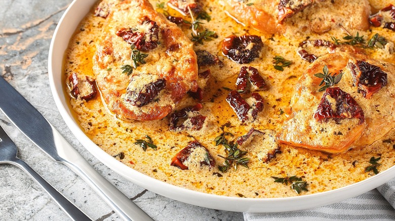 Marry me chicken in a white serving dish with a fork and knife