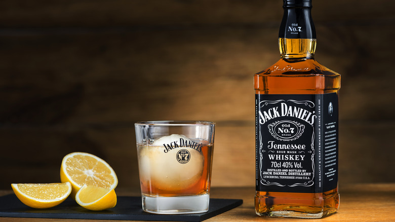 a bottle of Jack Daniel's next to a Jack Daniel's branded glass and lemon slices