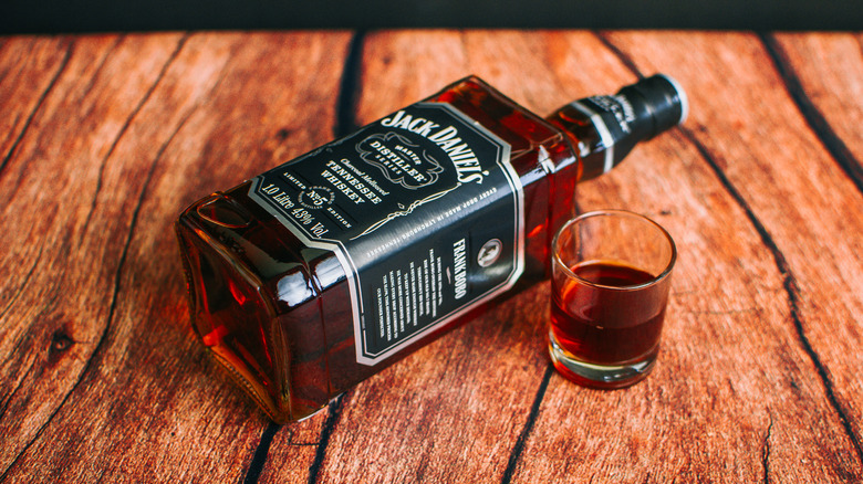 a 1 liter bottle of Jack Daniel's laying on its side next to a glass of whiskey on wood