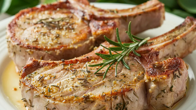 A plate of golden pork chops topped with herbs is photographed in close-up.
