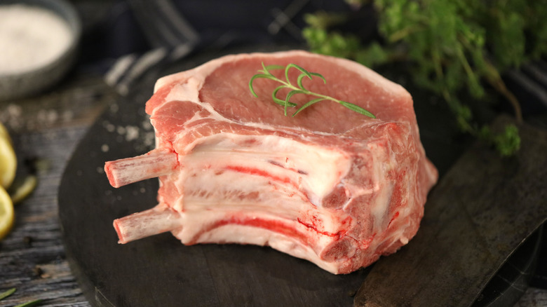 Bone-in pork chops on a wooden tray with herbs in the background.
