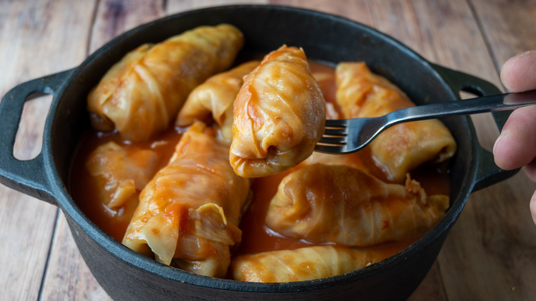 Stuffed cabbage rolls cooked in tomato sauce and served from a cast iron pot with a fork.