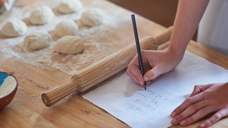person writing a recipe while baking