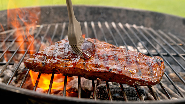 Applying BBQ sauce to food on a charcoal grill