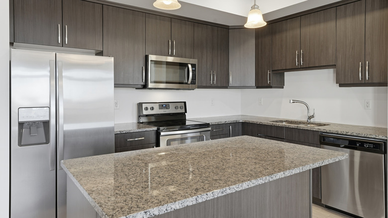 A modern neutral-colored kitchen with granite countertops and metallic appliances