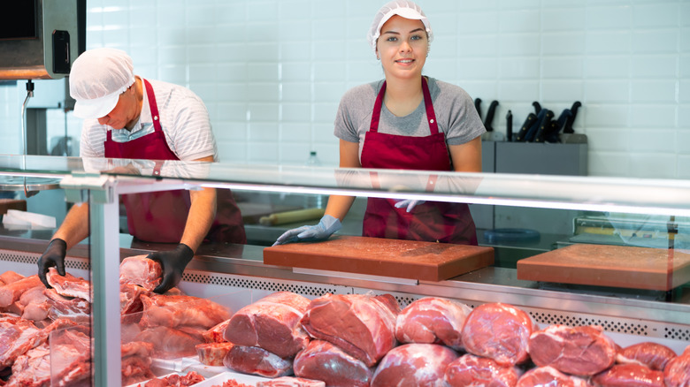 Butchers are seen behind a counter in a shop.