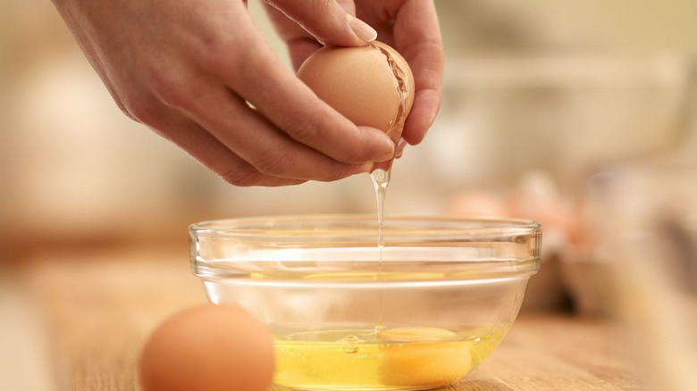 Hands cracking egg into a clear bowl