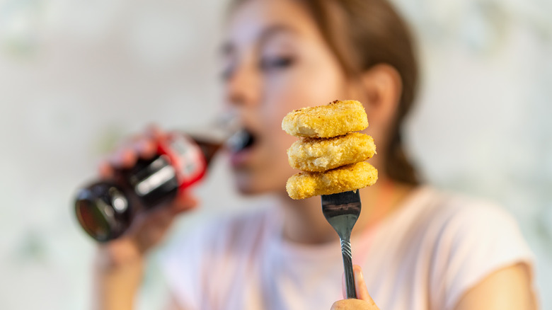 Person drinking cola soda and holding chicken nuggets on a fork