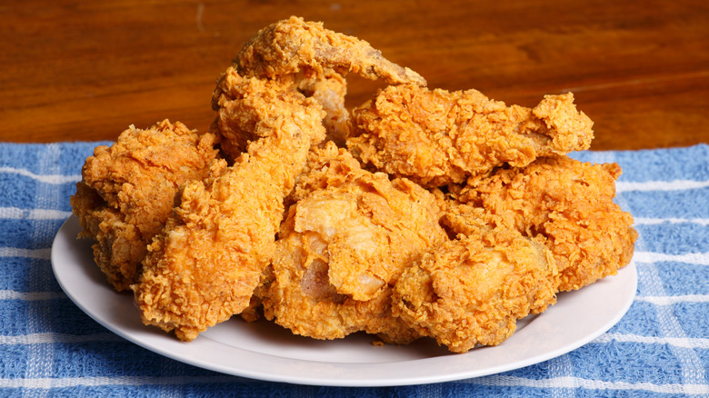 Plate of fried chicken on blue and white checkered cloth on wood surface.