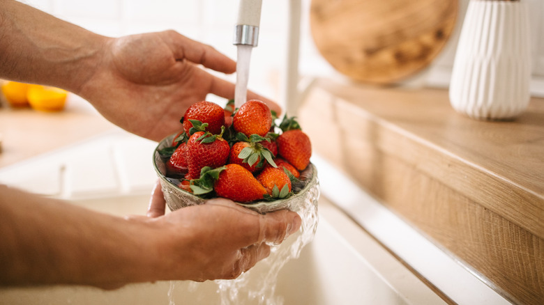 Hands holding a bowl with strawberries and washing them with clean water