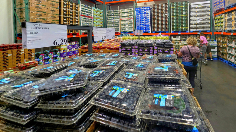 Pallets full of large containers of fresh blueberries sit in the produce section of a Costco as consumers shop.