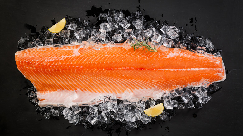 Slab of salmon resting on ice cubes with lemon wedges and a rosemary sprig