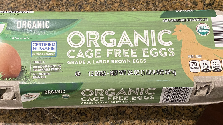 A carton of a dozen of Aldi's Simply Nature Organic Cage Free Eggs sits on a countertop. Beneath the product name are the words "Grade A Large Brown Eggs," and to the left and right are labels that say "Certified Humane" and "USDA Organic."