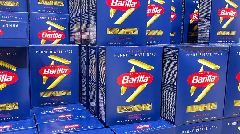 Boxes of Barilla penne rigate pasta lined on a store shelf.