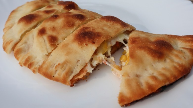 A cheese and vegetable calzone on a paper plate similar to calzones served at A-Pizza Mart in Seattle.