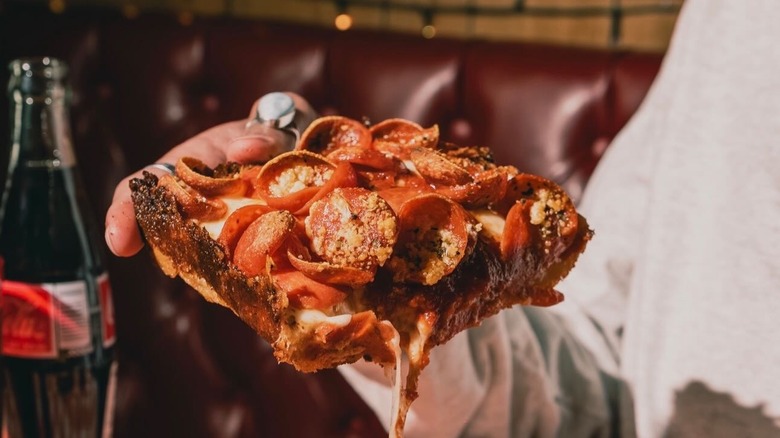 A person holding a slice of Detroit-style pizza at Ace's Pizza