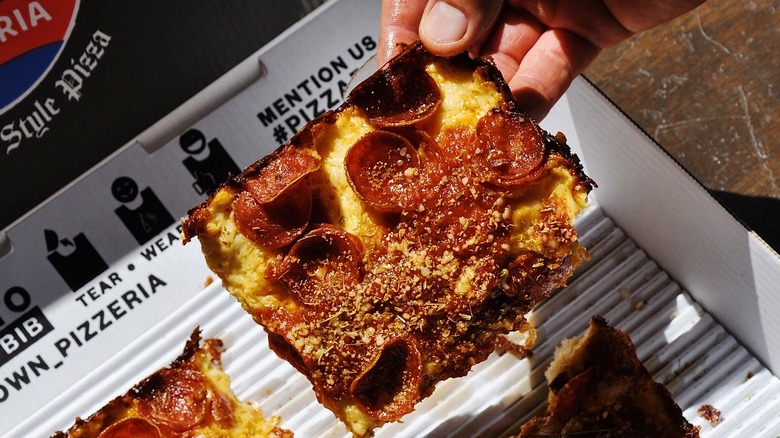 A person holding a slice of Detroit-style pizza from DTown Pizzeria