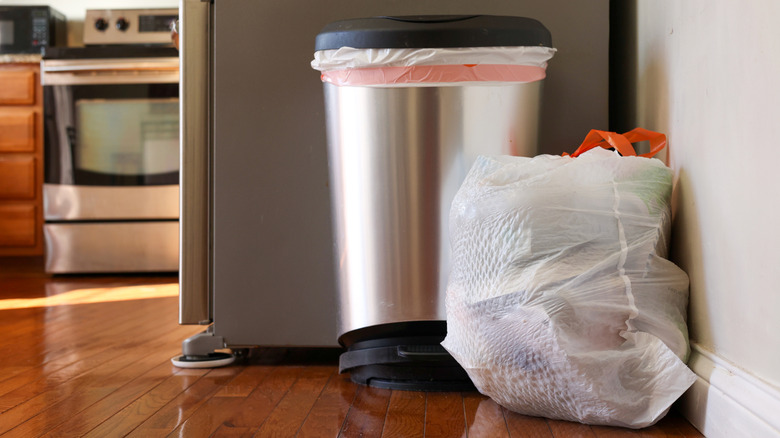 Full kitchen trash bag beside a trash can