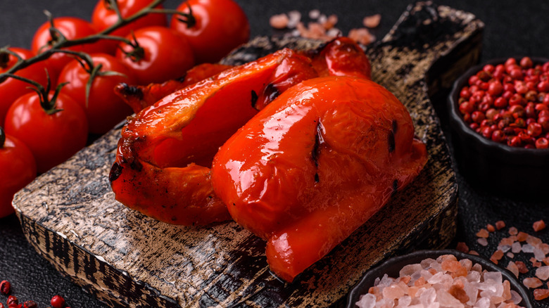 Grilled red bell peppers are arranged on a cutting board.