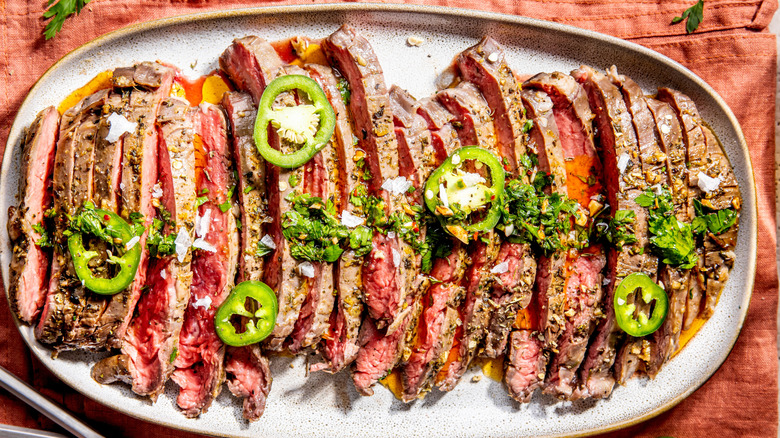 Sliced flank of steak on a platter garnished with coriander and jalipeños