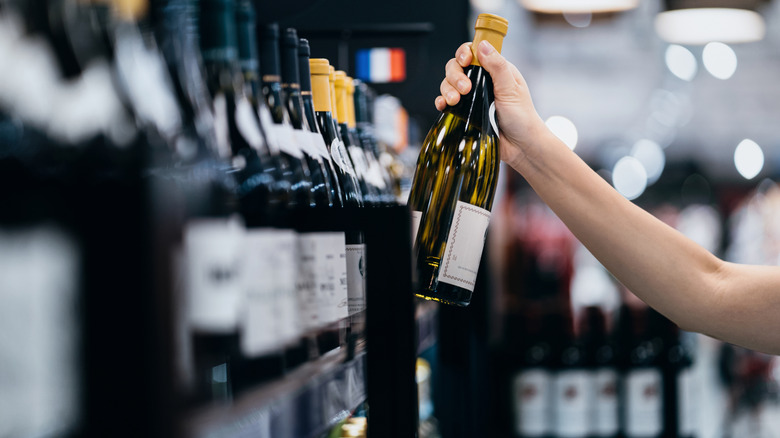 Woman taking a bottle of white wine off the shelf at a store
