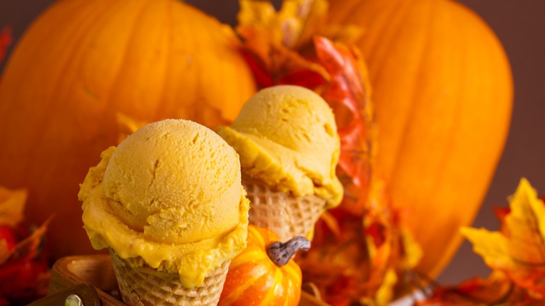 Waffle cones filled with pumpkin ice cream displayed in front of two pumpkins
