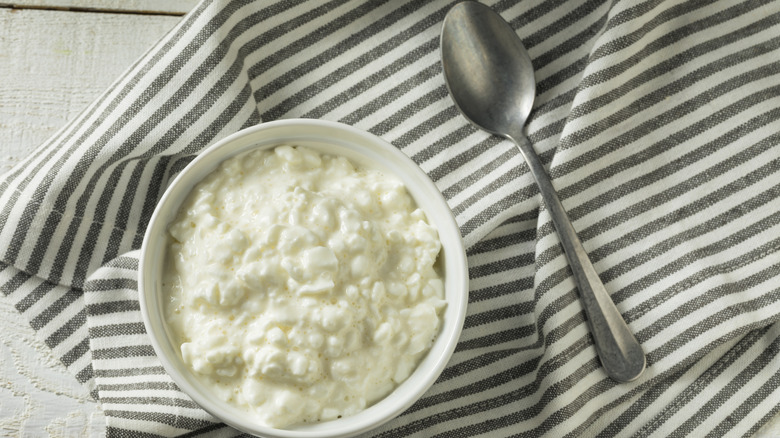 A bowl of cottage cheese sitting on a striped towel next to a spoon