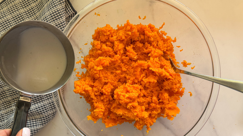 hand adding cream to bowl with sweet potatoes