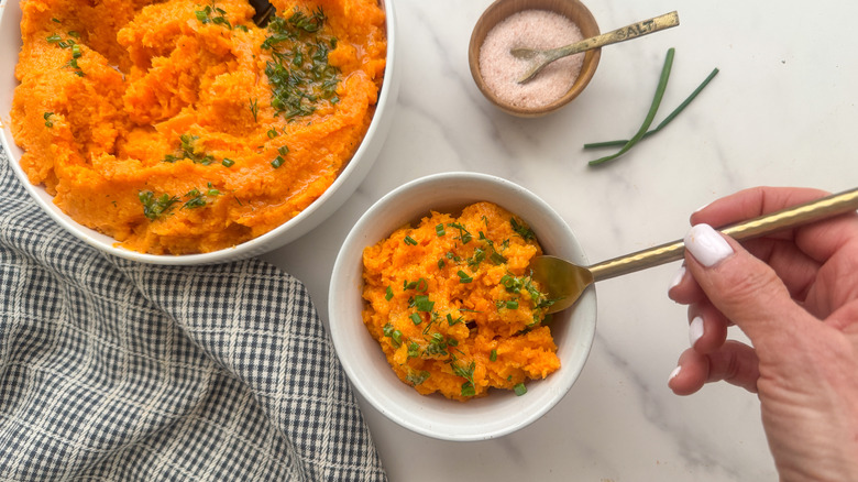 hand with fork in bowl of sweet potatoes