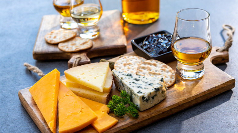 Whiskey with different kinds of cheese on a wooden board