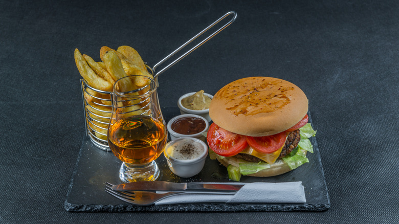 A burger and chips on a tray with a glass of whiskey.
