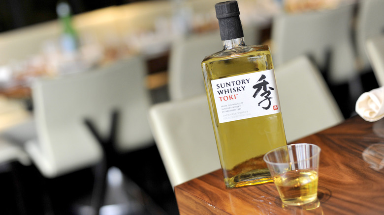 A bottle of Toki Suntory Whisky sitting on a wooden table next to a small glass of the whiskey