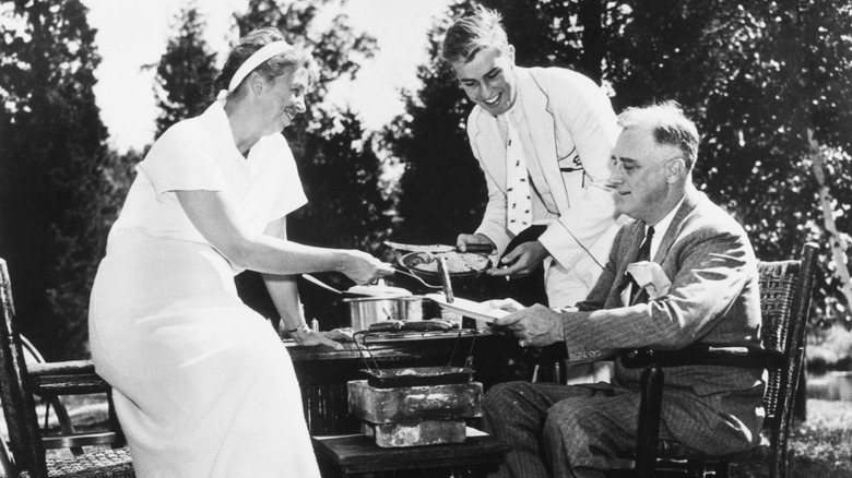 Eleanor Roosevelt serves a hot dog to Franklin D. Roosevelt while their son, Franklin Jr., looks on
