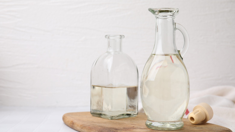 Two cler bottles of white vinegar on a wooden board.