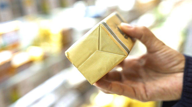 Hand holding a one-pound package of butter in the refrigerated section of a grocery store