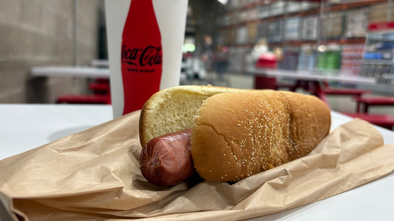 Close up of a Costco hotdog in front of Coca-cola paper cup on table in store.