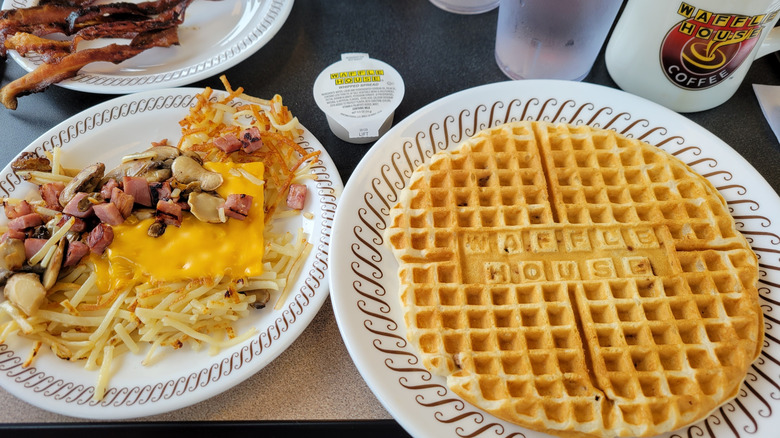 Plates of hash browns and waffles on a diner table at a Waffle House.