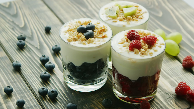 Three glasses of berry yogurt parfaits on wood table.