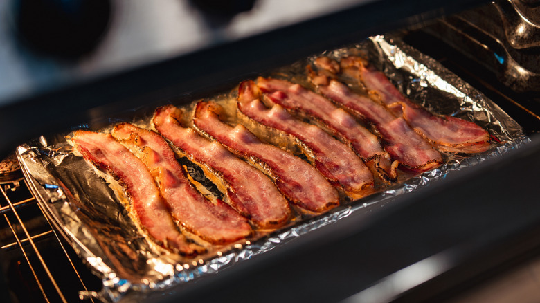 Bacon cooking on a foil-lined sheet pan in an oven