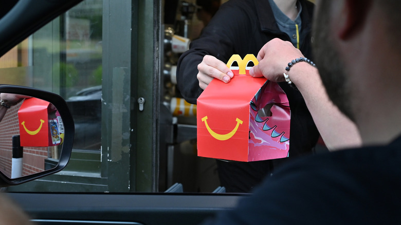 Person in a McDonald's drive thru receiving a Happy Meal from a McDonald's employee