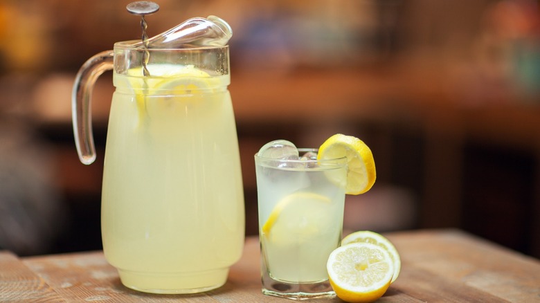 Jug of lemonade next to glass of lemonade with lemons