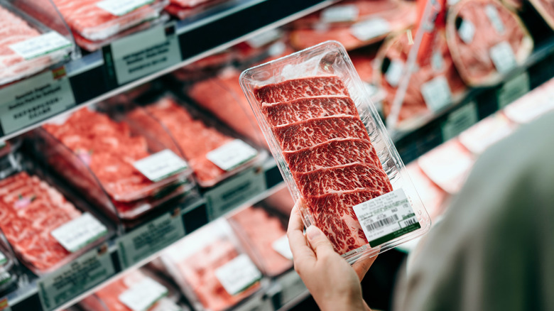 Person holding packaged raw meat in a grocery store
