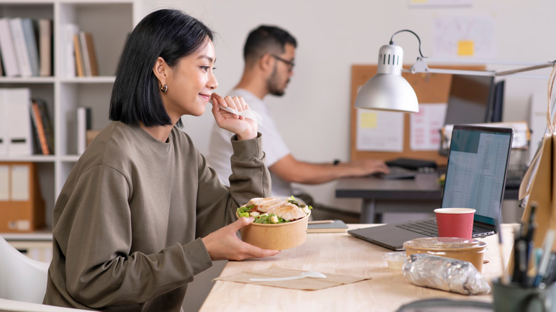 Smiling woman in long sleeved shirt eating lunch while working