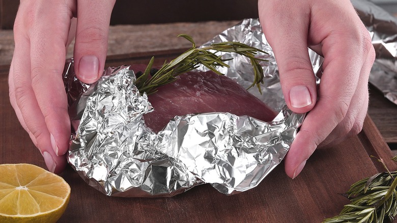 person rolling fish and rosemary in aluminum foil