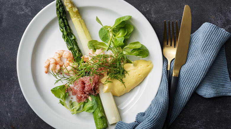 Asparagus and shrimp plated with hollandaise sauce next to a blue napkin and gold silverware.