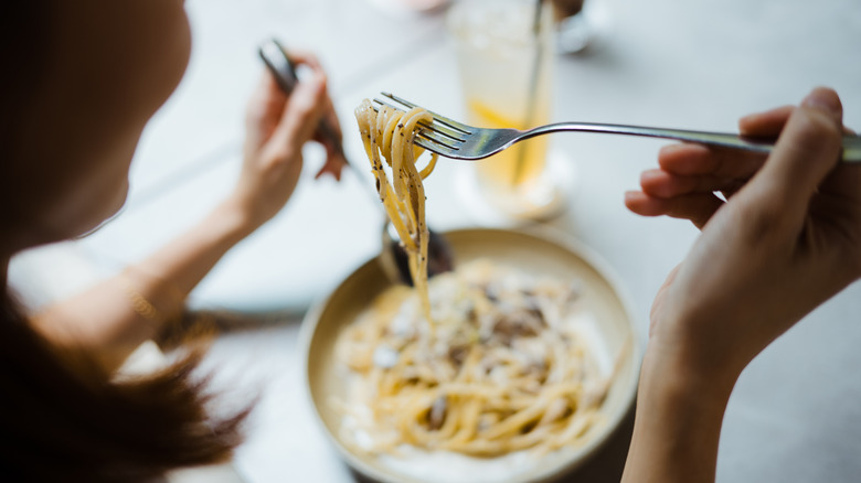 Woman enjoy eating a spaghetti carbonara in Italian restaurant with a fork.