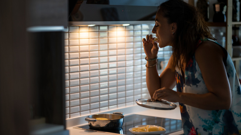 Woman eating a meal at night while standing over the stove.