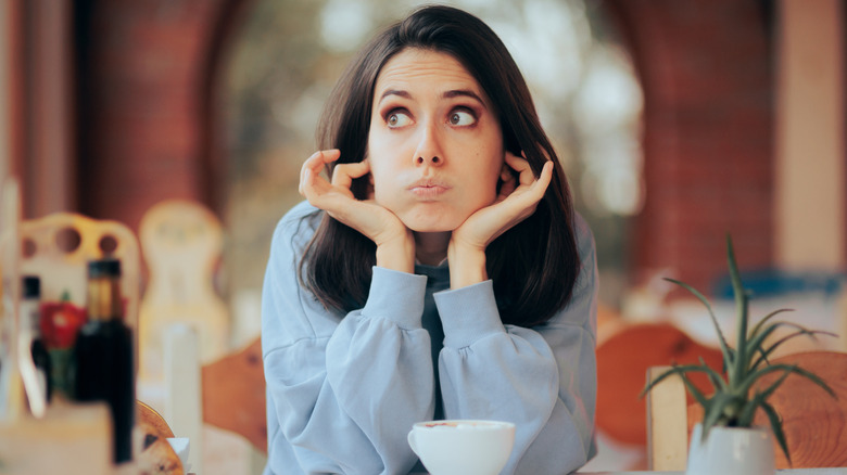 A woman at a restaurant table blocking her ears from loud music.