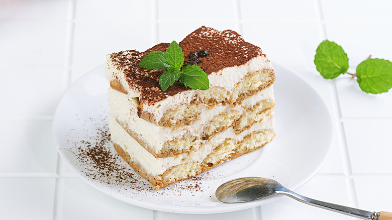 A slice of tiramisu with a sprig of mint on a plate.